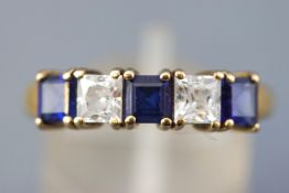 A yellow metal half hoop ring. Set with synthetic blue sapphire and colourless cubic zirconia.