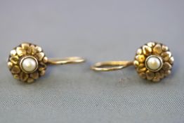 A yellow metal pair of earrings. Each centrally set with a seed pearl. Hook fittings.