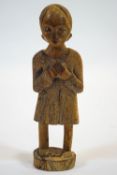 A small African carved wooden fetish figure, with hands clasped, standing on an oval base,