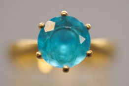 A yellow metal single stone ring. Set with a round faceted cut intense blue topaz.