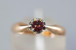 A yellow and white metal single stone ring. Set with a round faceted cut garnet (untested).