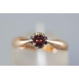 A yellow and white metal single stone ring. Set with a round faceted cut garnet (untested).