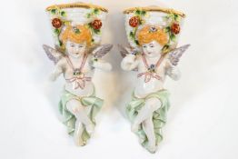 A pair of German wall pockets in the form of putti each with a basket