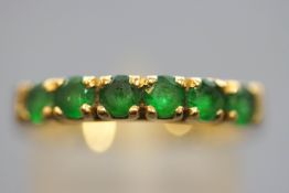 A yellow metal half hoop ring. Set with six round faceted cut green stones.