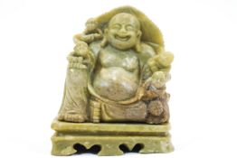 An Asian soapstone carved figure of a Buddha and attendants seated on a rocky ground,