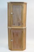 A pair of pine hanging corner cabinets, the panelled doors enclosing shelving, on plinth bases,