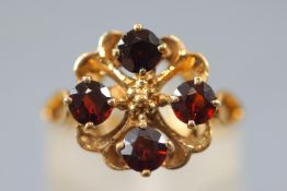 A yellow metal dress ring set with four round faceted cut garnets.