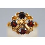 A yellow metal dress ring set with four round faceted cut garnets.