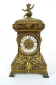 A brass clock with enamelled dial, the wasted case with putto finial,