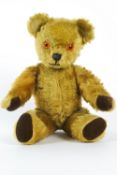 A plush teddy bear with a growler and bell, with brown velvet paws and amber coloured eyes,