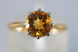 A yellow and white metal single stone ring set with a round faceted cut citrine quartz.