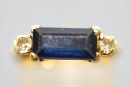 A yellow metal dress ring set with a rectangular cut dark blue sapphire