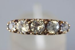 A yellow metal half hoop ring. Set with five graduated round faceted cut colourless zircon.