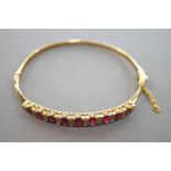 A yellow metal half hoop bangle set with graduated commercial quality rubies