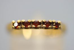 A yellow metal half hoop ring set with five round faceted cut garnets. Untested - Stamped 9ct.