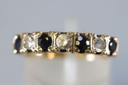 A yellow metal half hoop ring set with dark blue sapphires and cubic zirconia.