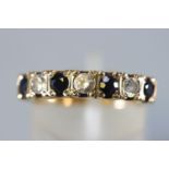 A yellow metal half hoop ring set with dark blue sapphires and cubic zirconia.