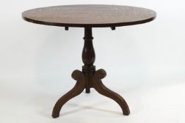 An early 19th century provincial oak tripod table with round tilt top over a turned baluster