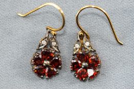 A yellow and white metal pair of flower design drop earrings each set with heart cut garnets