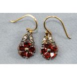 A yellow and white metal pair of flower design drop earrings each set with heart cut garnets