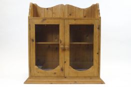 A pine hanging cupboard with two glazed doors enclosing one shelf, on a stepped glazed plinth base,