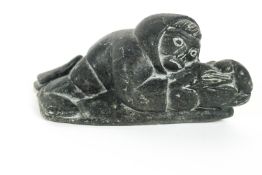 A modern carved stone sculpture of a reclining Inuit figure, indistinct incised marks to underside,