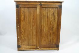 A pine cupboard with two panelled doors enclosing fixed shelves,