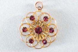 A yellow metal abstract floral design pendant set with round faceted cut rhodolite garnets.