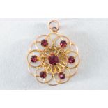 A yellow metal abstract floral design pendant set with round faceted cut rhodolite garnets.