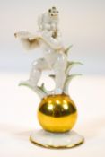 A Hutschenreuther porcelain figure of a cupid playing a flute standing on a gilt ball on flared