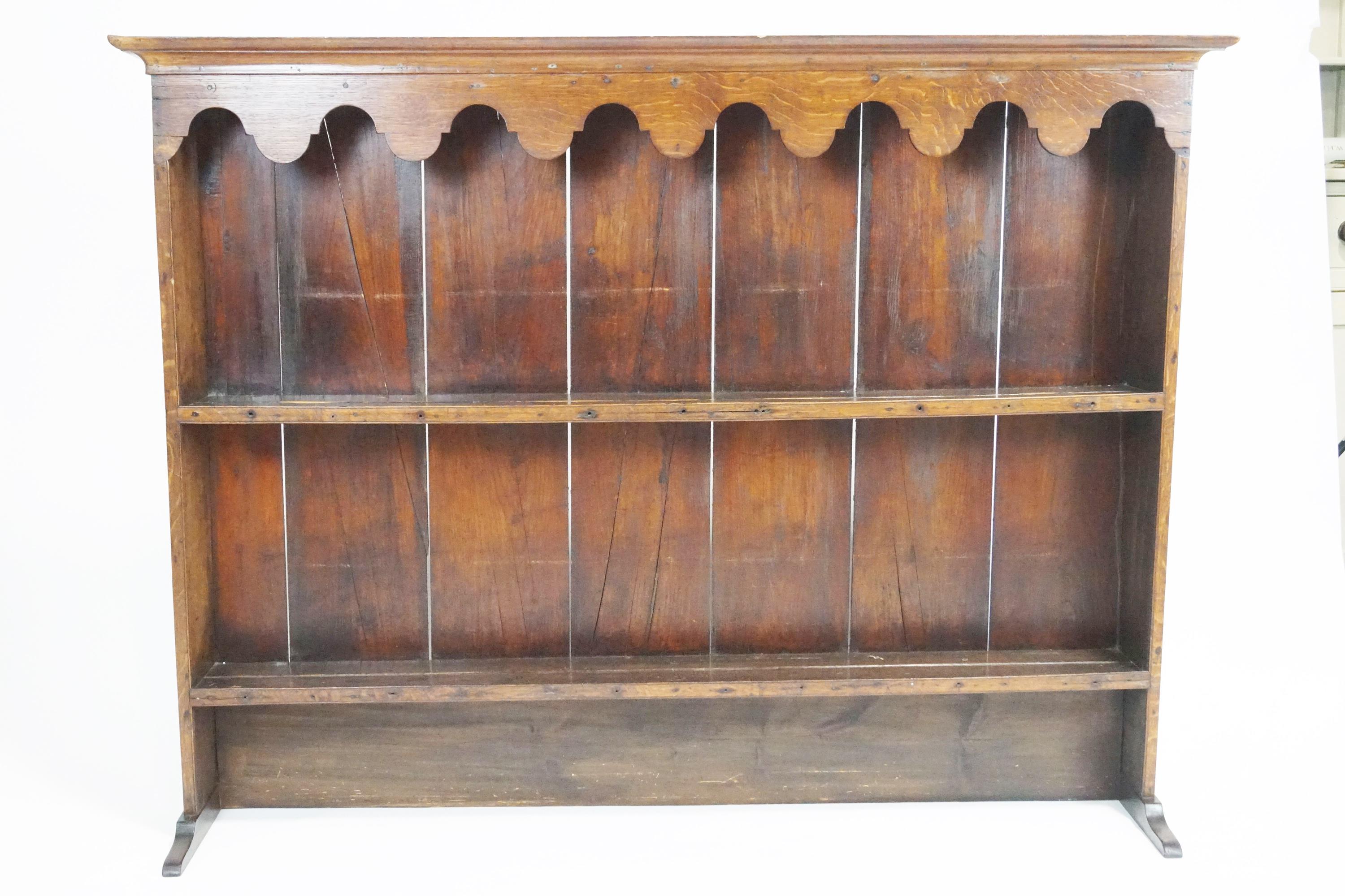An oak plate rack, with two shelves below a scrolled hanging apron and moulded top,