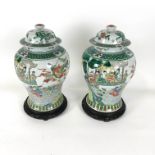 A pair of baluster famille verte vases (one cracked) and covers, painted with figures in pavilions,