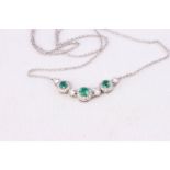 A white metal necklace having a centrepiece design and set with emeralds and diamonds.