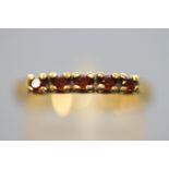 A yellow metal half hoop ring set with five round faceted cut garnets. Untested - Stamped 9ct.