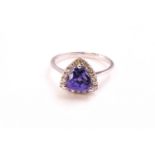A white metal cluster ring. Set with a trilliant cut tanzanite and surrounded by round cut diamonds.