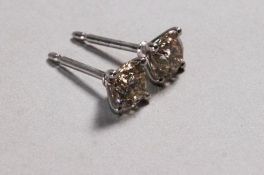 A white metal pair of single stone stud earrings each set with a round brilliant cut diamond