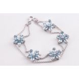 A white metal bracelet having five fixed flowers each set with pear cut aquamarines