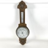 An oak aneroid barometer, with decorative flower head to the top,