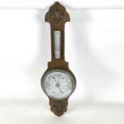 An oak aneroid barometer, with decorative flower head to the top,