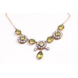 A yellow and white metal necklace having an ornate floral centrepiece design set with peridot,
