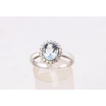 A white metal cluster ring principally set with an oval faceted cut aquamarine