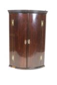 A mahogany corner cupboard, the curved hinged doors inlaid with stringing,