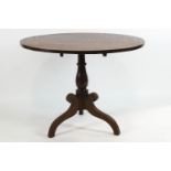 An early 19th century provincial oak tripod table with round tilt top over a turned baluster