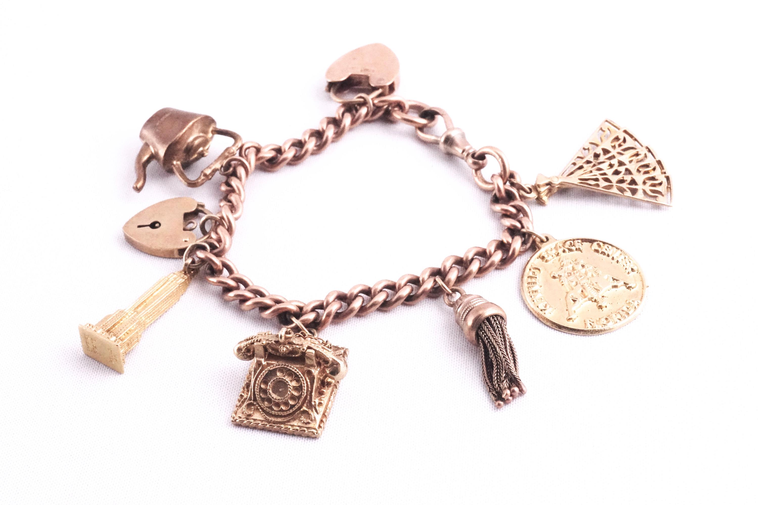 A rose gold curb link charm bracelet with padlock and safety chain having six assorted charms