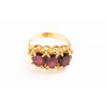 A yellow metal dress ring. Set with three oval faceted cut garnets