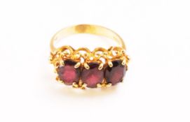 A yellow metal dress ring. Set with three oval faceted cut garnets