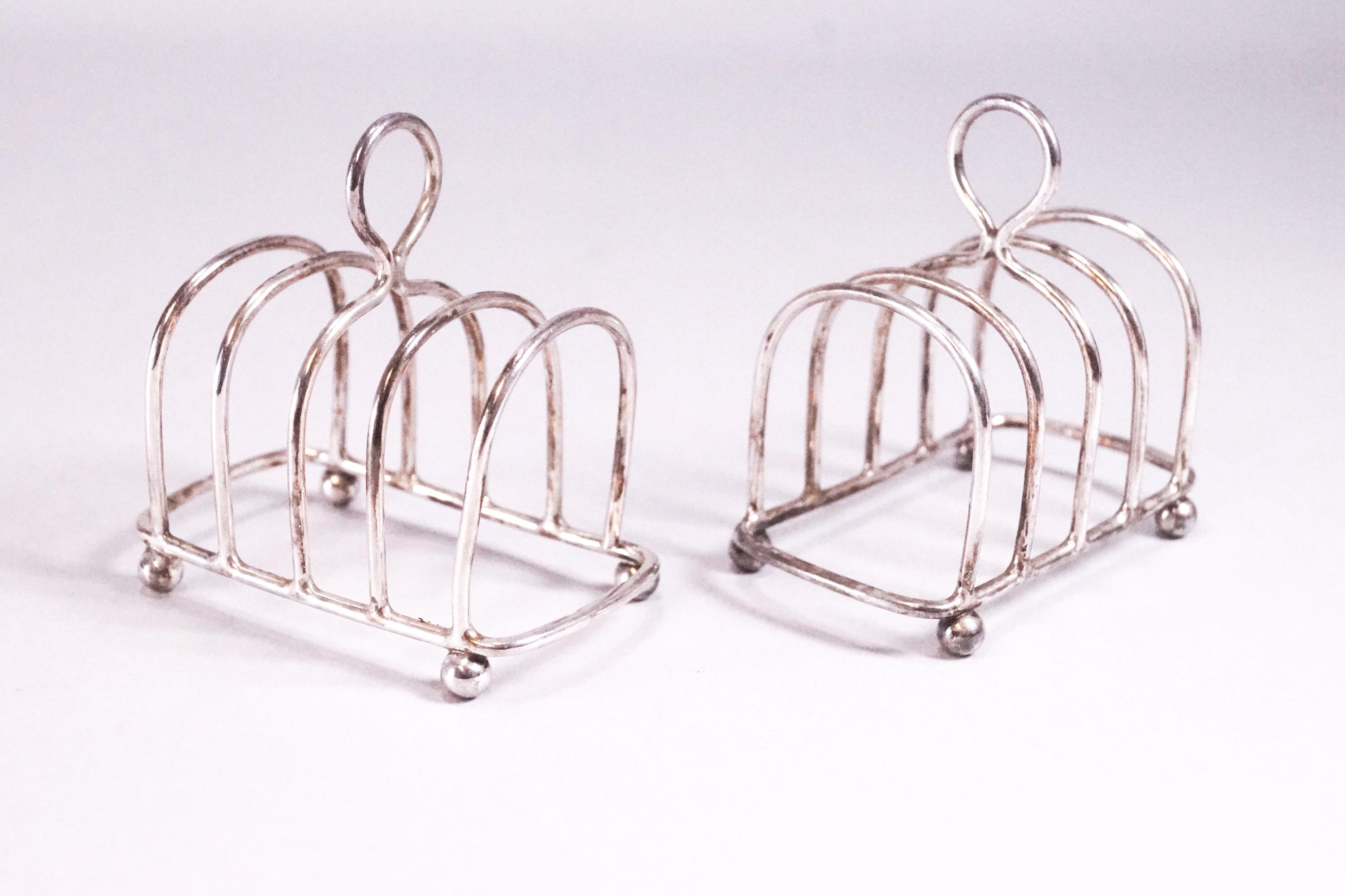 A pair of silver miniature form plain round arch toast racks with loop handles, raised on ball feet,