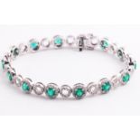 A white metal bracelet set with fourteen round faceted cut emeralds