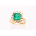 A yellow metal cluster ring principally set with a square step cut emerald