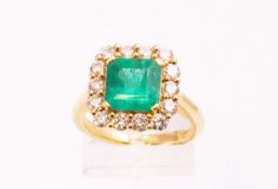 A yellow metal cluster ring principally set with a square step cut emerald